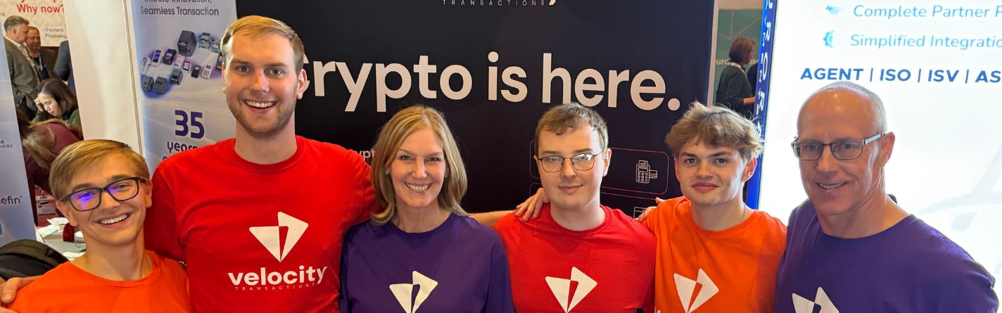 The Velocity Transactions team at a trade show booth announcing "Crypto is here."
